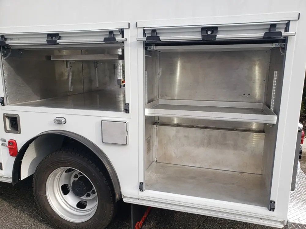 Exterior view of small fire truck showing cab, body compartments, and wheel/tire area.