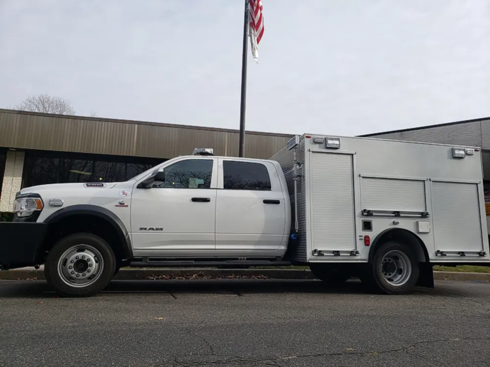 Exterior view of small fire truck showing cab, body compartments, and wheel/tire area.