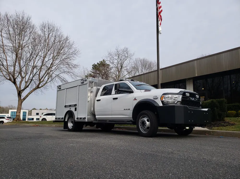 Exterior view of small fire truck showing cab, body compartments, and wheel/tire area.