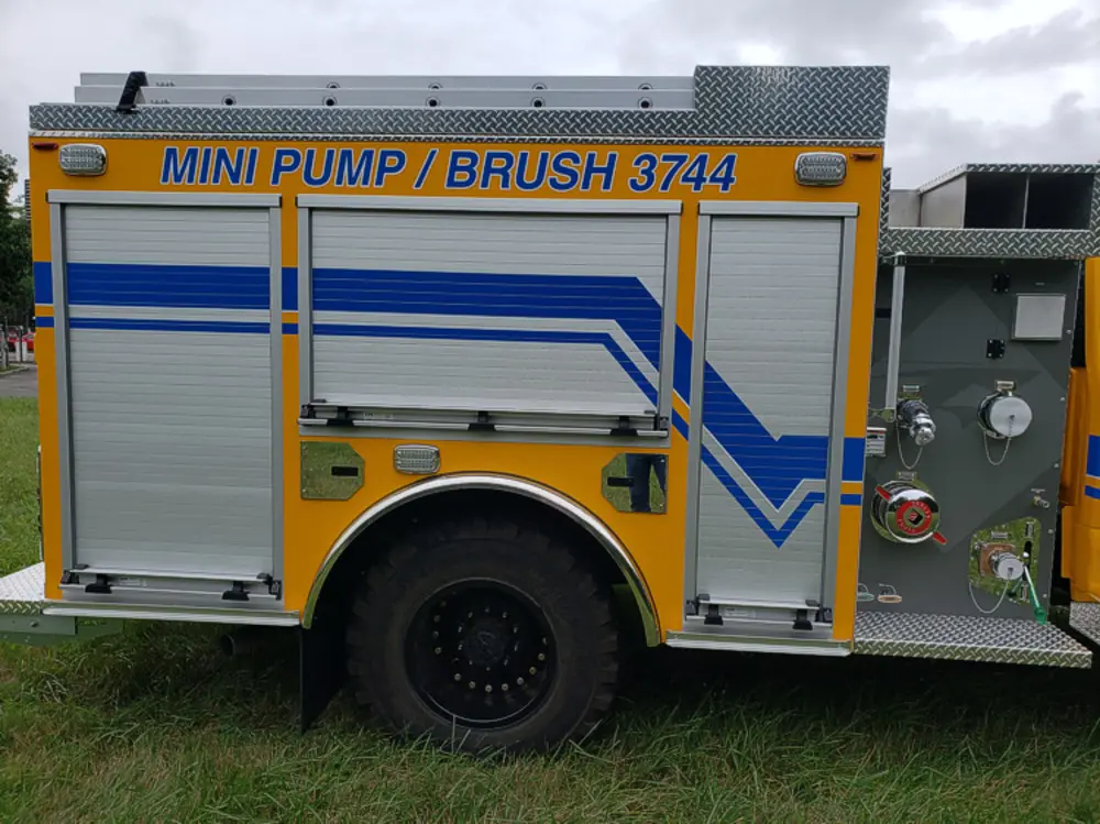 Exterior view of small fire truck showing cab, body compartments, and wheel/tire area.
