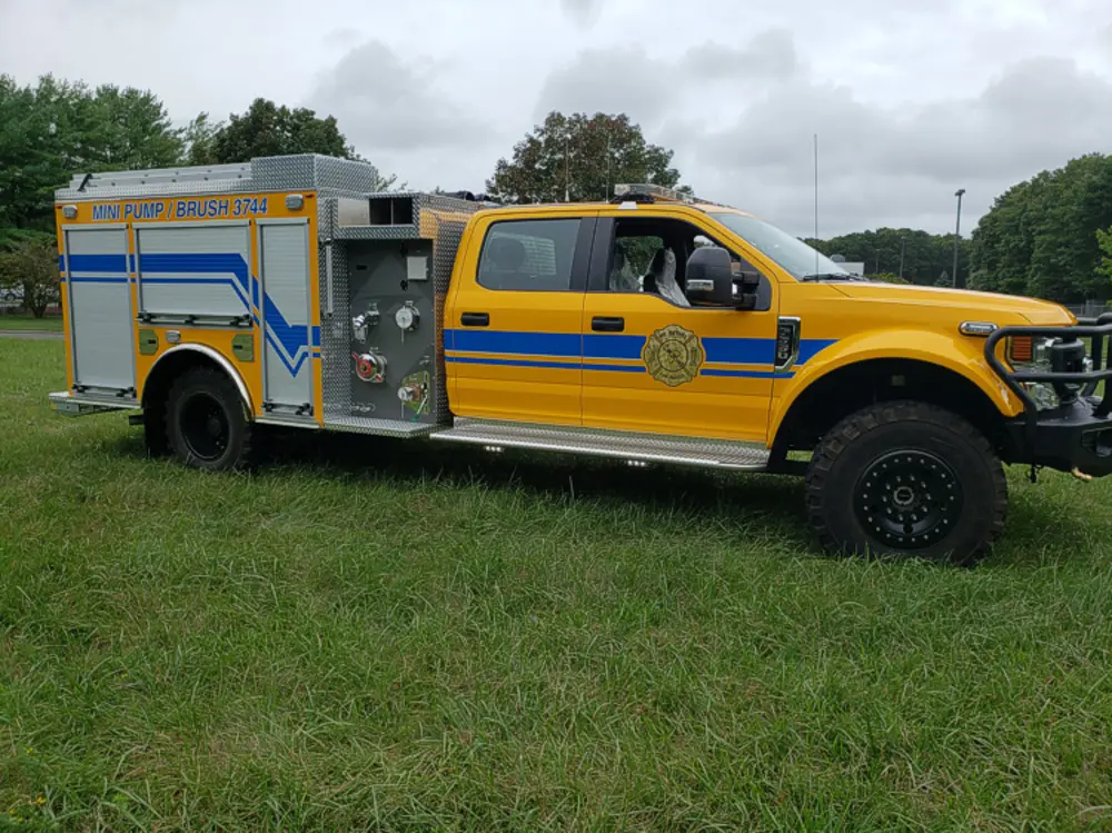 Exterior view of small fire truck showing cab, body compartments, and wheel/tire area.