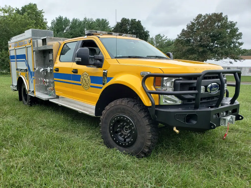 Exterior view of small fire truck showing cab, body compartments, and wheel/tire area.