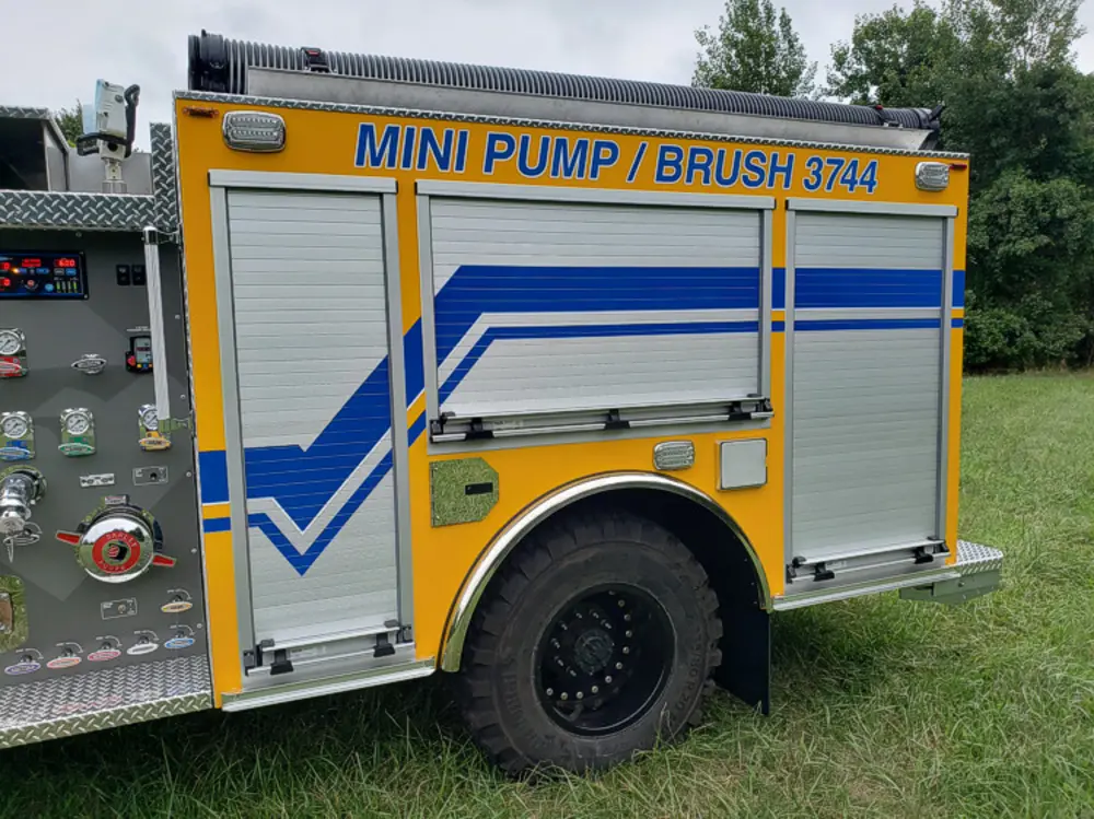 Exterior view of small fire truck showing cab, body compartments, and wheel/tire area.