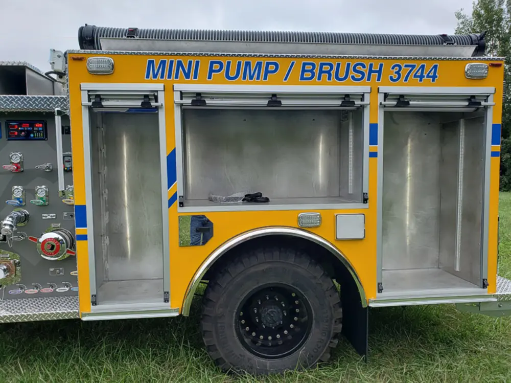 Exterior view of small fire truck showing cab, body compartments, and wheel/tire area.