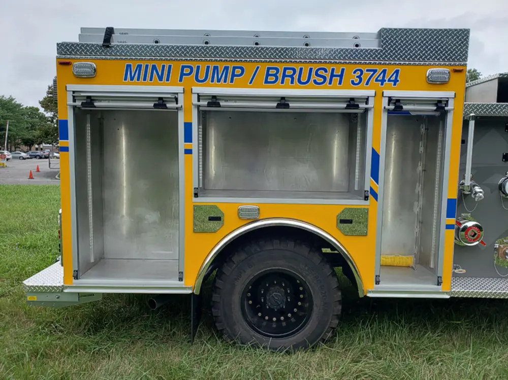 Exterior view of small fire truck showing cab, body compartments, and wheel/tire area.