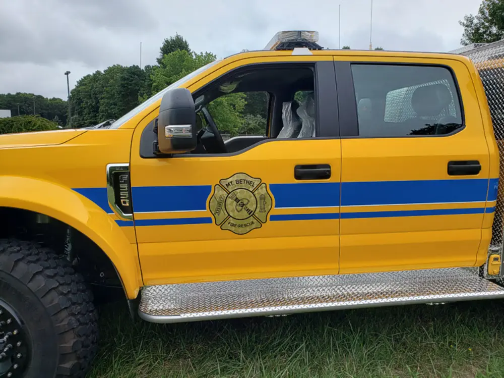 Exterior view of small fire truck showing cab, body compartments, and wheel/tire area.