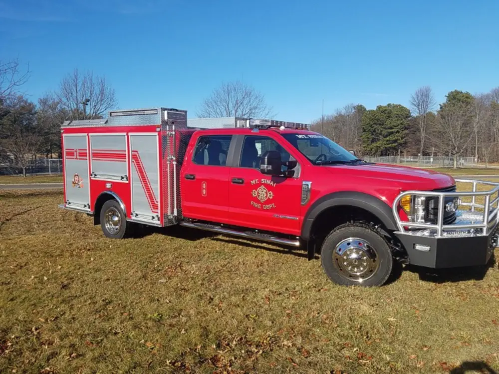 Exterior view of small fire truck showing cab, body compartments, and wheel/tire area.