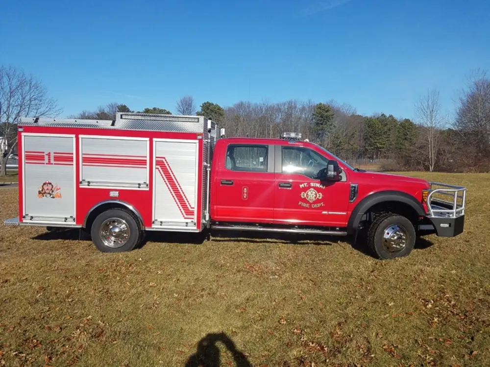 Exterior view of small fire truck showing cab, body compartments, and wheel/tire area.