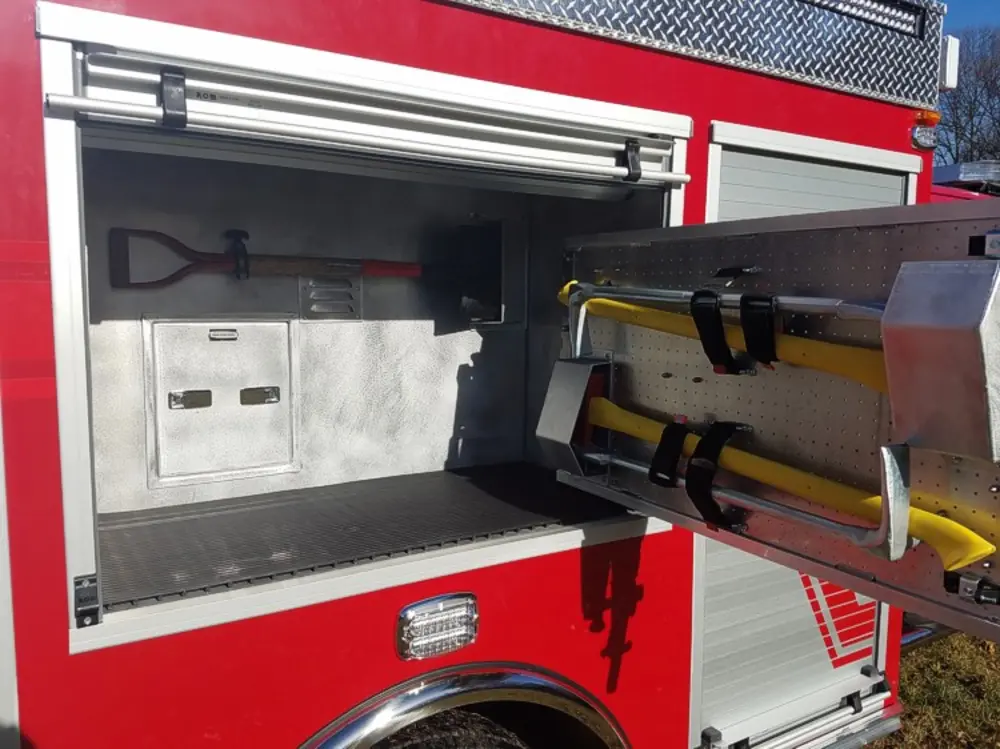 Exterior view of small fire truck showing cab, body compartments, and wheel/tire area.