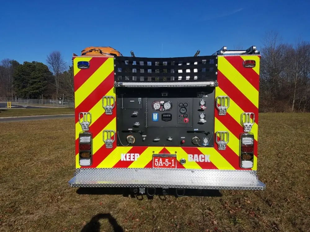 Exterior view of small fire truck showing cab, body compartments, and wheel/tire area.