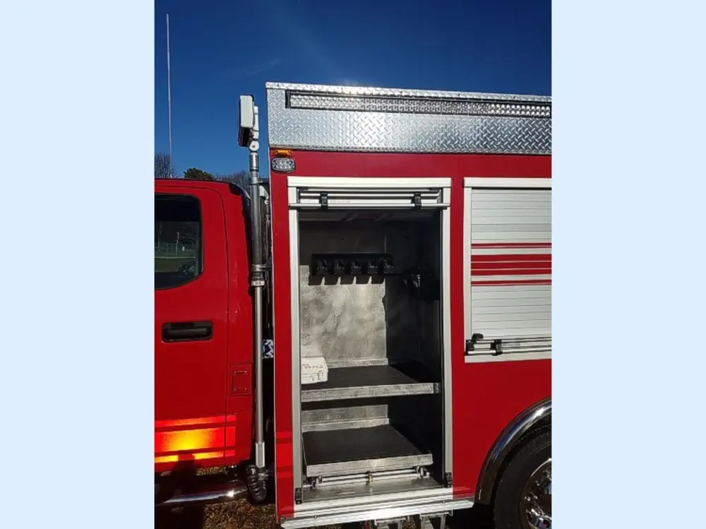 Exterior view of small fire truck showing cab, body compartments, and wheel/tire area.