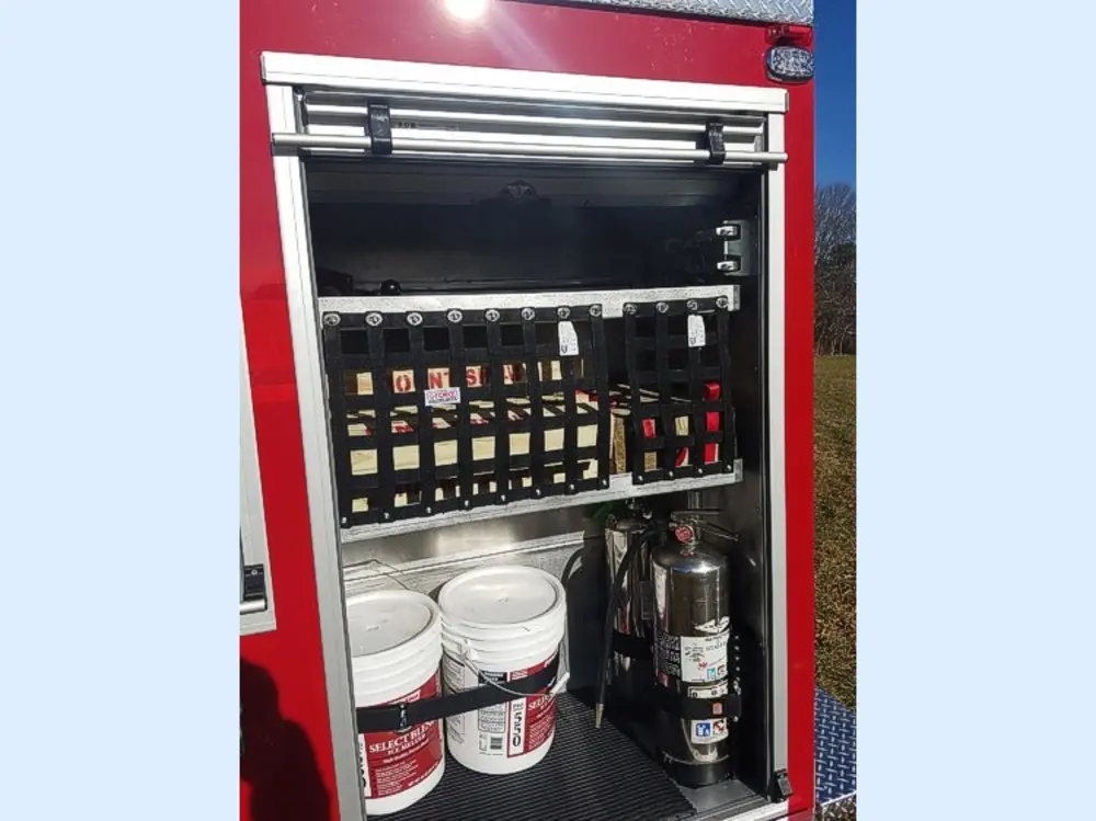 Exterior view of small fire truck showing cab, body compartments, and wheel/tire area.