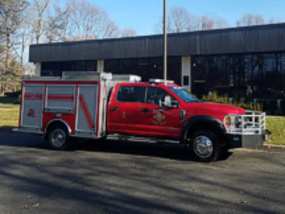 Exterior view of small fire truck showing cab, body compartments, and wheel/tire area.