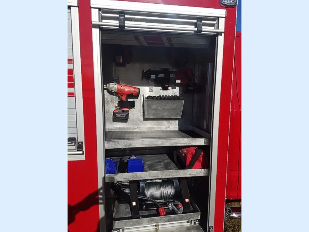 Exterior view of small fire truck showing cab, body compartments, and wheel/tire area.