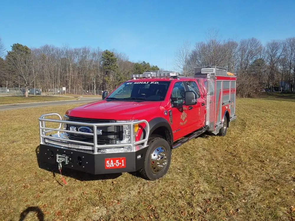 Exterior view of small fire truck showing cab, body compartments, and wheel/tire area.