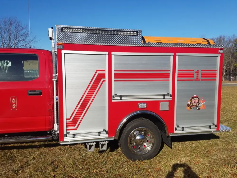 Exterior view of small fire truck showing cab, body compartments, and wheel/tire area.