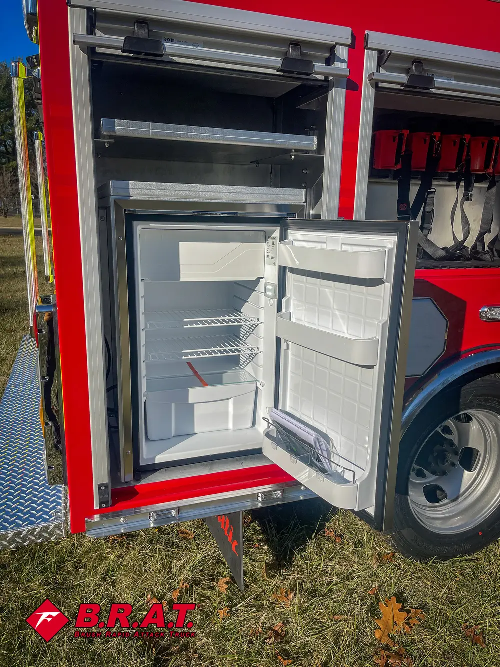 Narrow side compartment with small white mini-fridge and shelf.