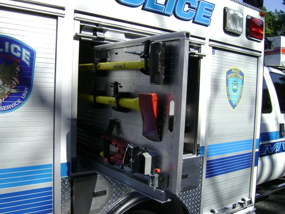 Exterior view of small fire truck showing cab, body compartments, and wheel/tire area.