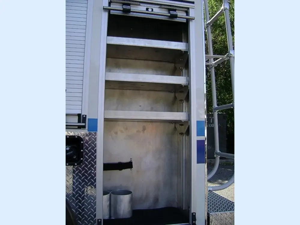 Exterior view of small fire truck showing cab, body compartments, and wheel/tire area.