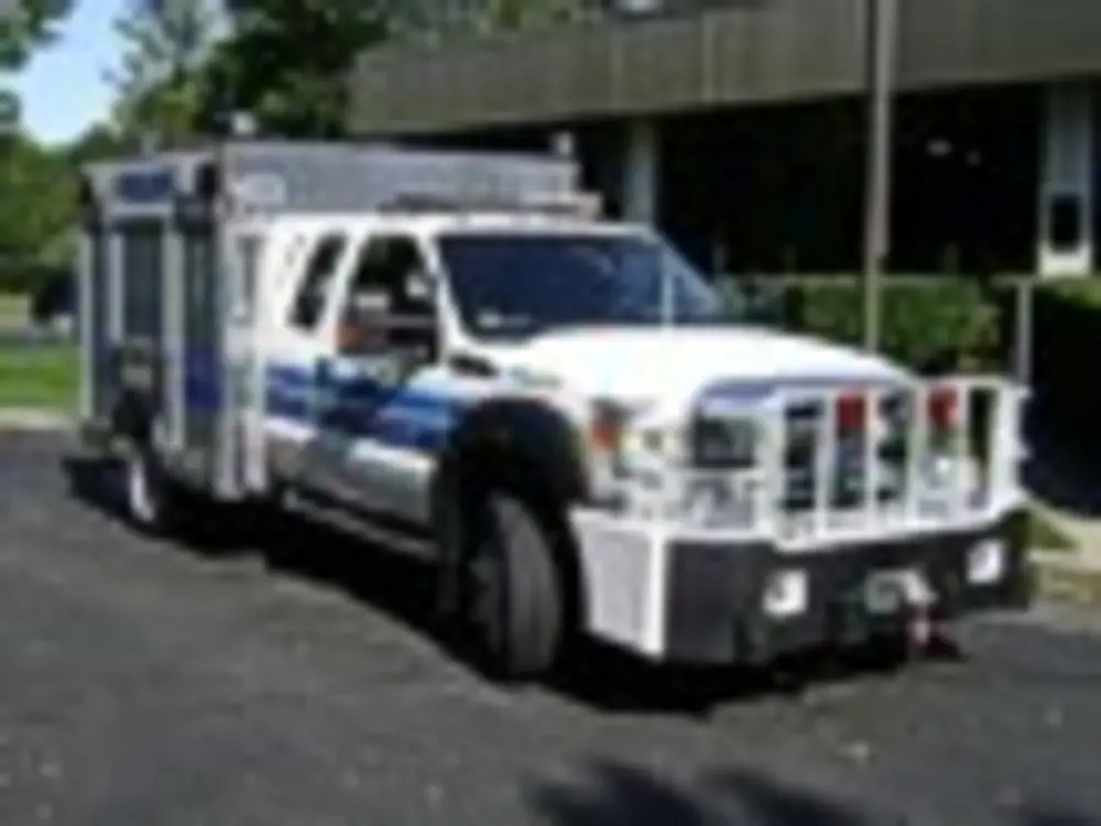 Exterior view of small fire truck showing cab, body compartments, and wheel/tire area.