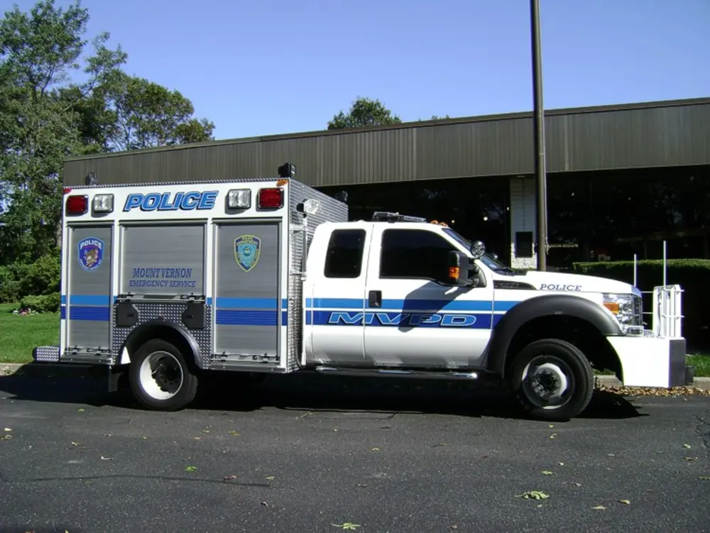 Exterior view of small fire truck showing cab, body compartments, and wheel/tire area.