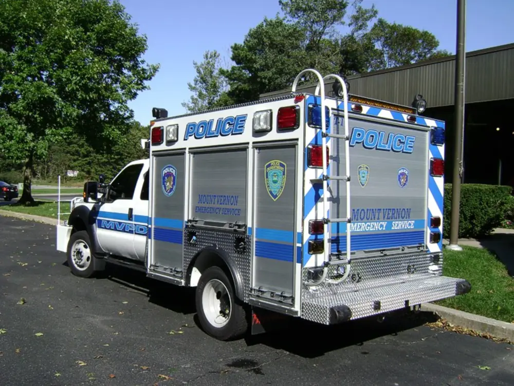 Exterior view of small fire truck showing cab, body compartments, and wheel/tire area.