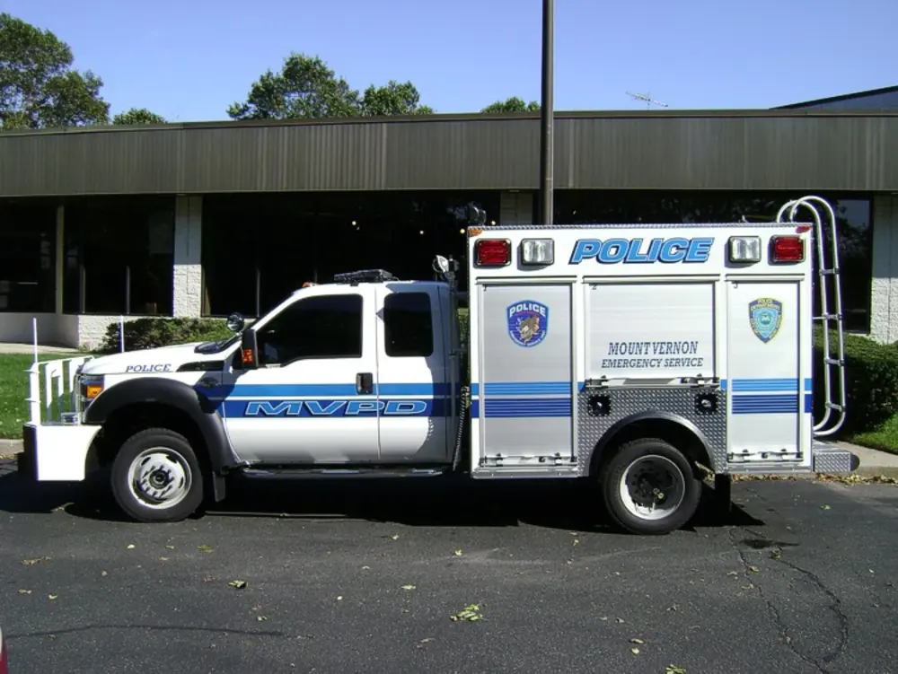 Exterior view of small fire truck showing cab, body compartments, and wheel/tire area.
