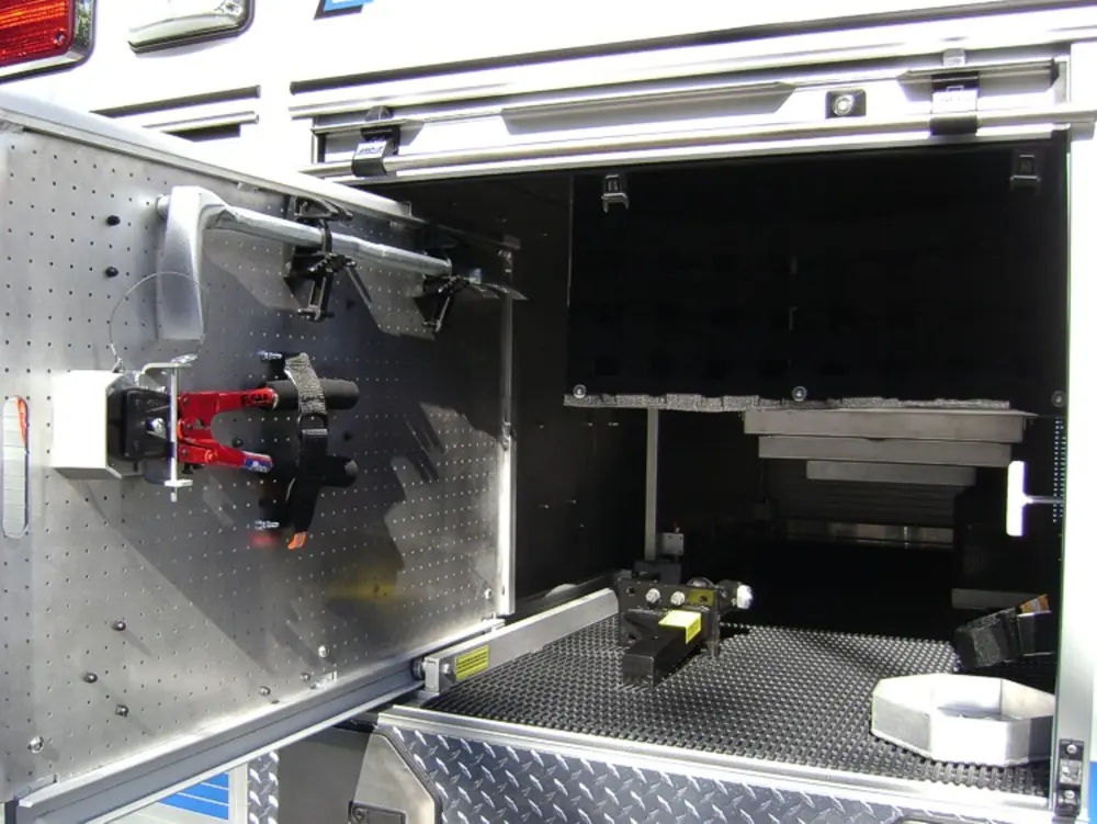 Exterior view of small fire truck showing cab, body compartments, and wheel/tire area.