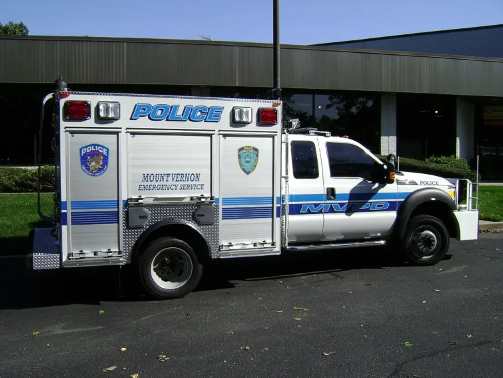 Exterior view of small fire truck showing cab, body compartments, and wheel/tire area.