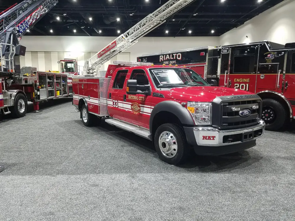Exterior view of small fire truck showing cab, body compartments, and wheel/tire area.