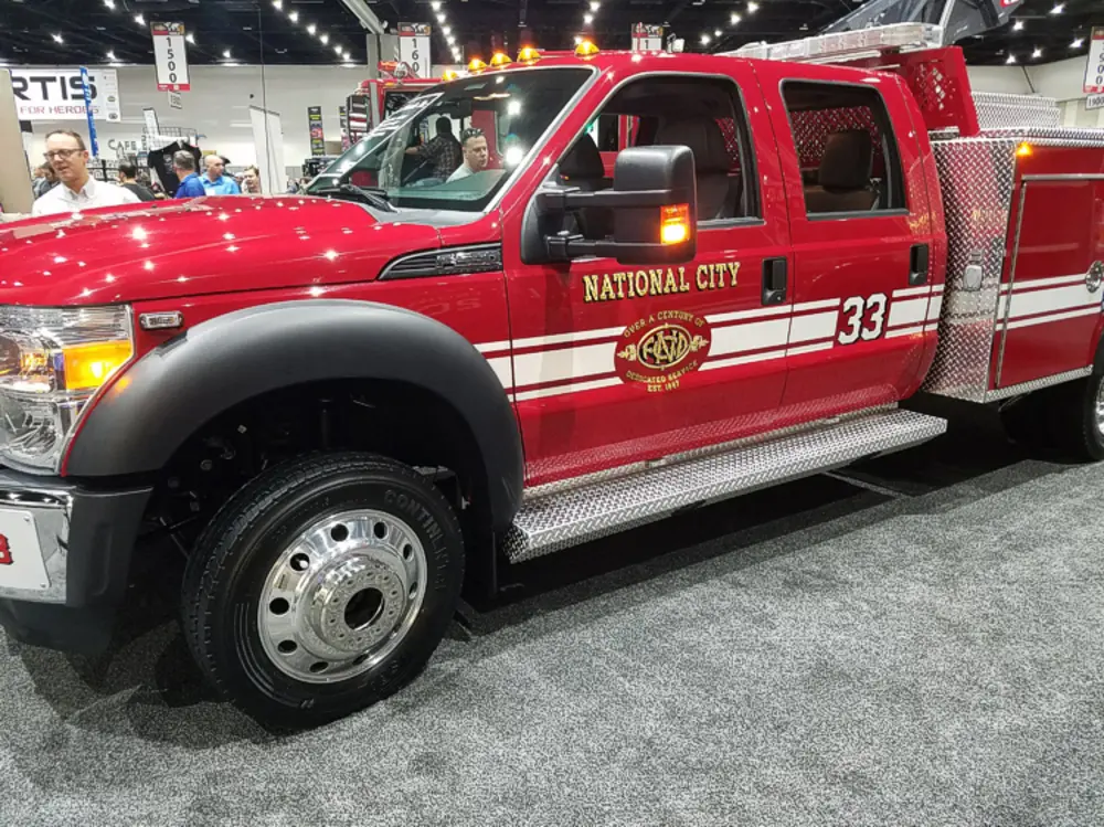 Exterior view of small fire truck showing cab, body compartments, and wheel/tire area.