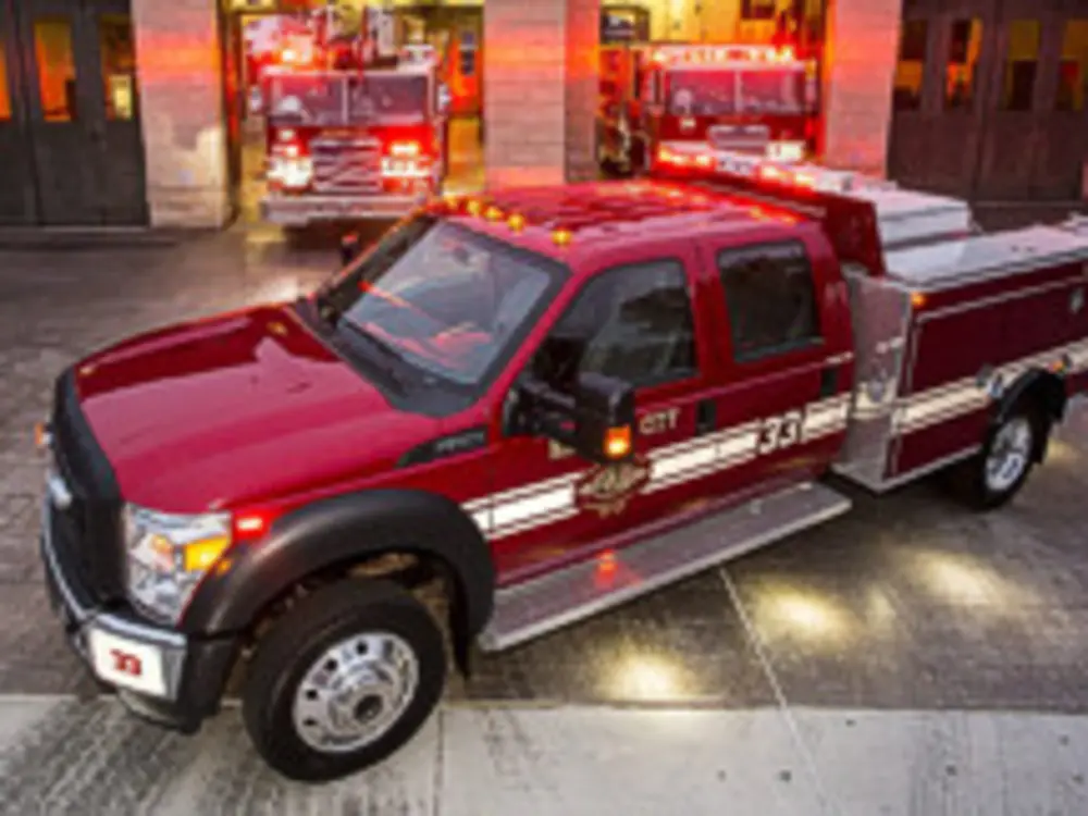Exterior view of small fire truck showing cab, body compartments, and wheel/tire area.