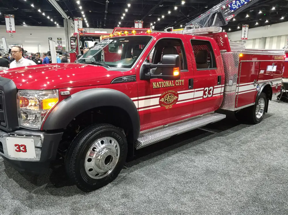 Exterior view of small fire truck showing cab, body compartments, and wheel/tire area.
