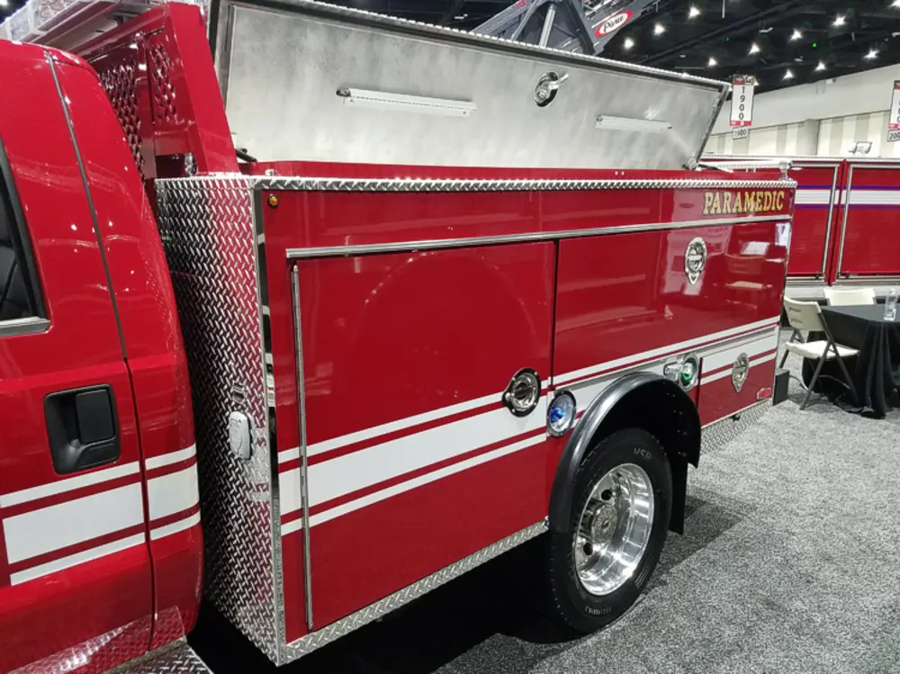 Exterior view of small fire truck showing cab, body compartments, and wheel/tire area.