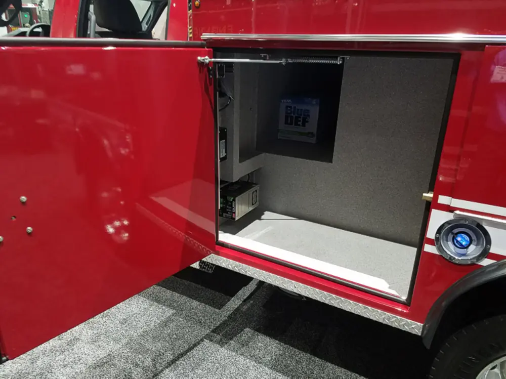 Exterior view of small fire truck showing cab, body compartments, and wheel/tire area.