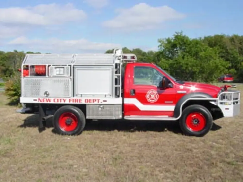 Exterior view of small fire truck showing cab, body compartments, and wheel/tire area.