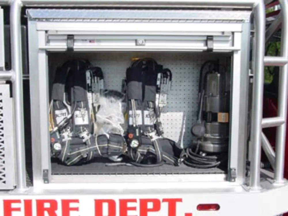 Exterior view of small fire truck showing cab, body compartments, and wheel/tire area.