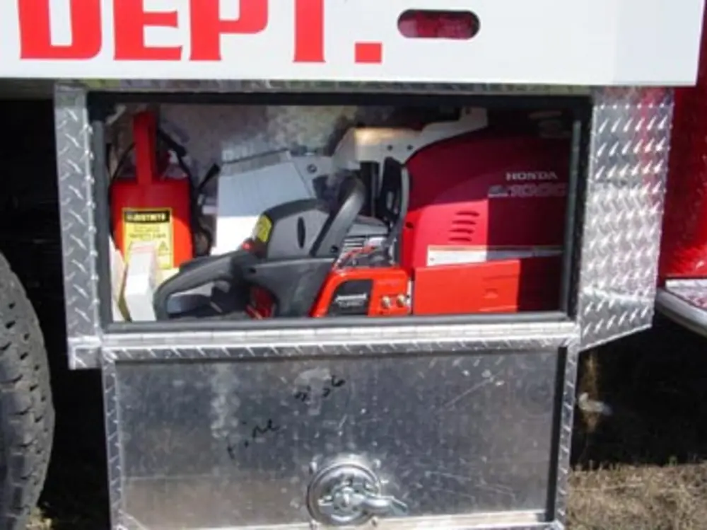 Exterior view of small fire truck showing cab, body compartments, and wheel/tire area.