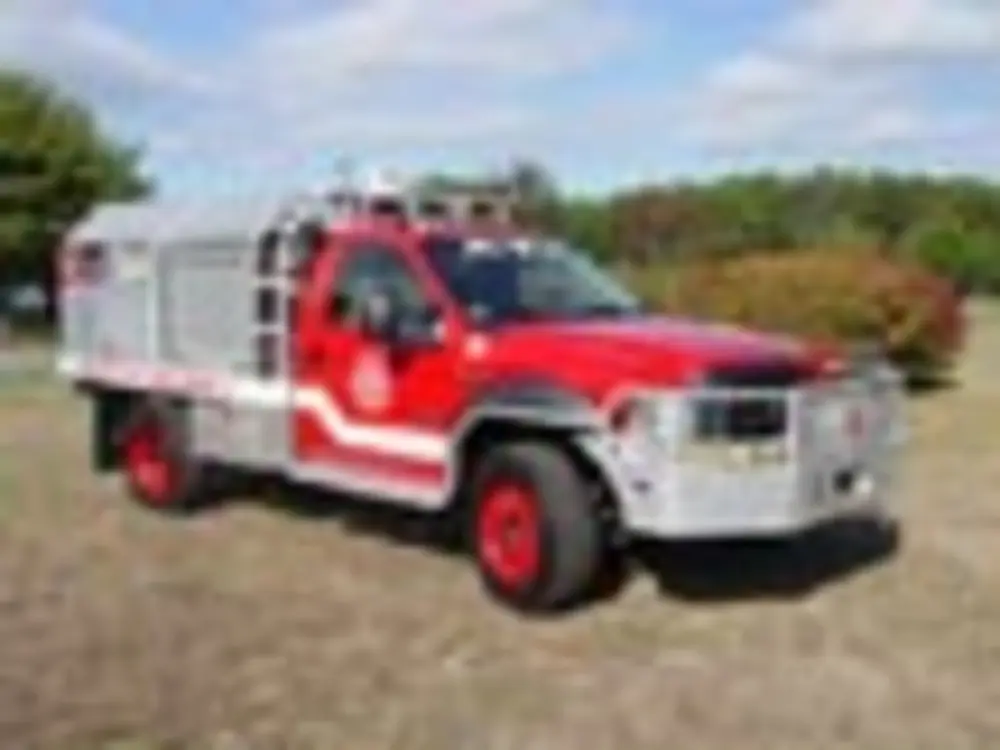 Exterior view of small fire truck showing cab, body compartments, and wheel/tire area.