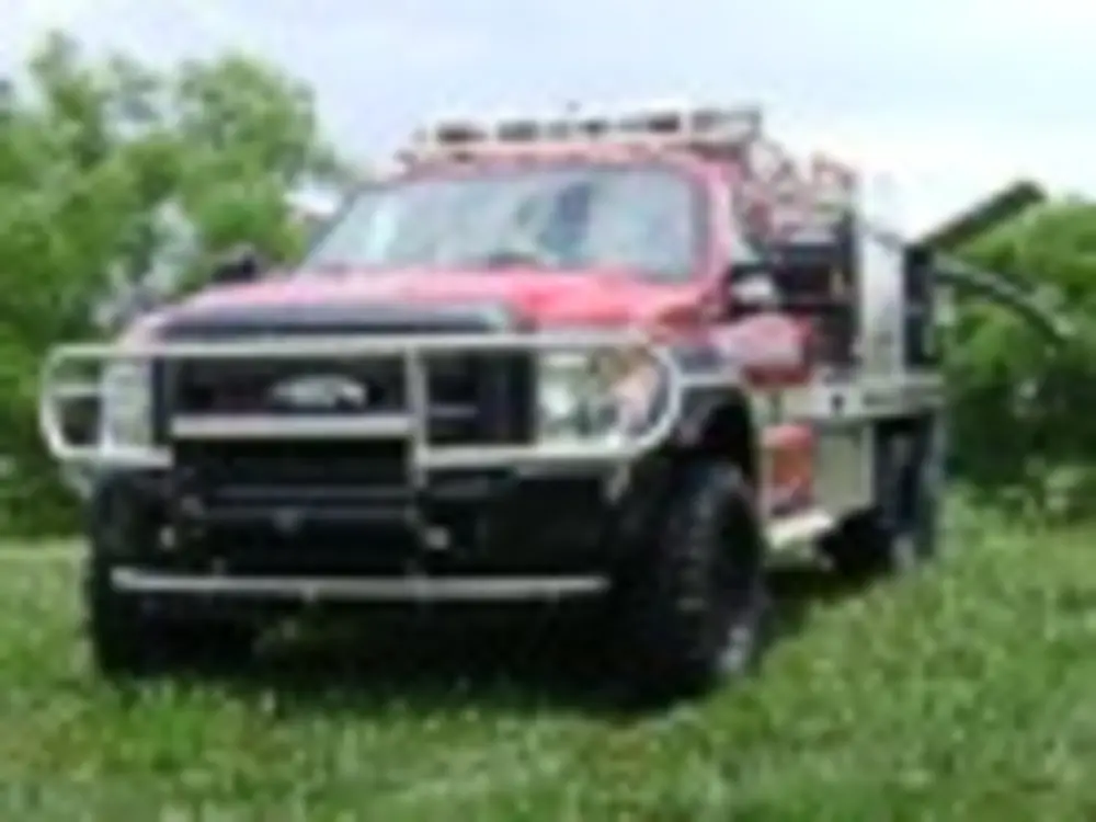 Exterior view of small fire truck showing cab, body compartments, and wheel/tire area.