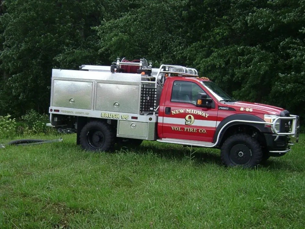 Exterior view of small fire truck showing cab, body compartments, and wheel/tire area.