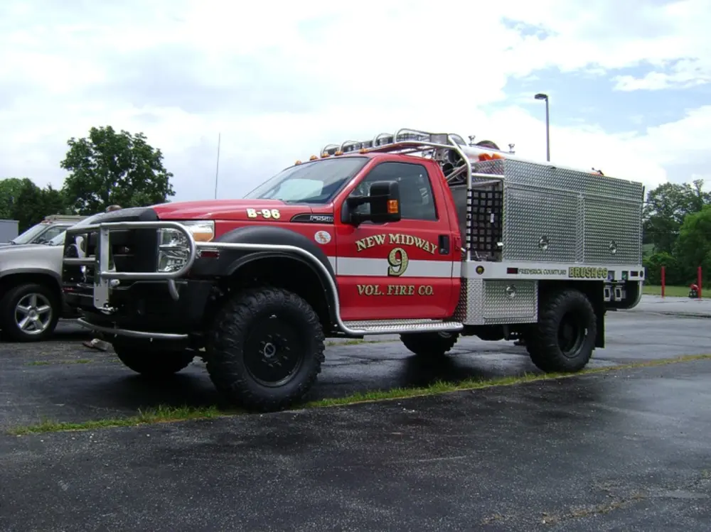 Exterior view of small fire truck showing cab, body compartments, and wheel/tire area.