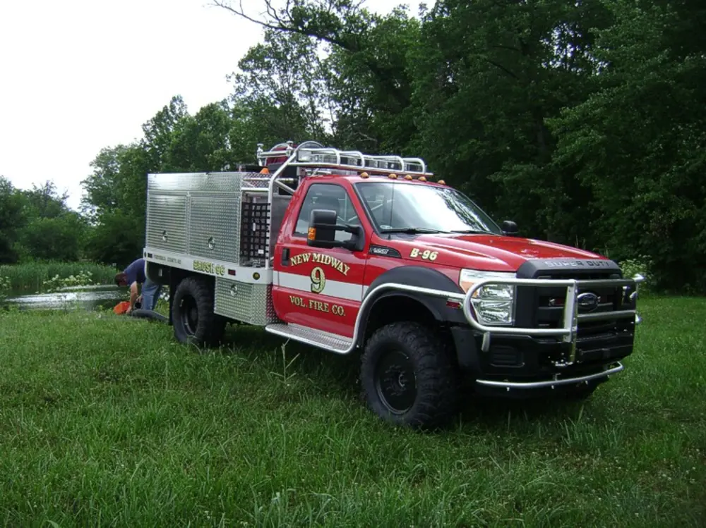 Exterior view of small fire truck showing cab, body compartments, and wheel/tire area.