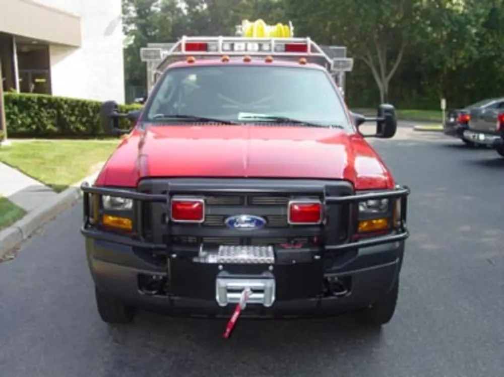 Exterior view of small fire truck showing cab, body compartments, and wheel/tire area.