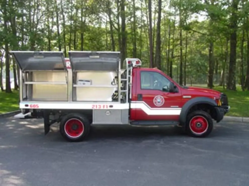 Exterior view of small fire truck showing cab, body compartments, and wheel/tire area.