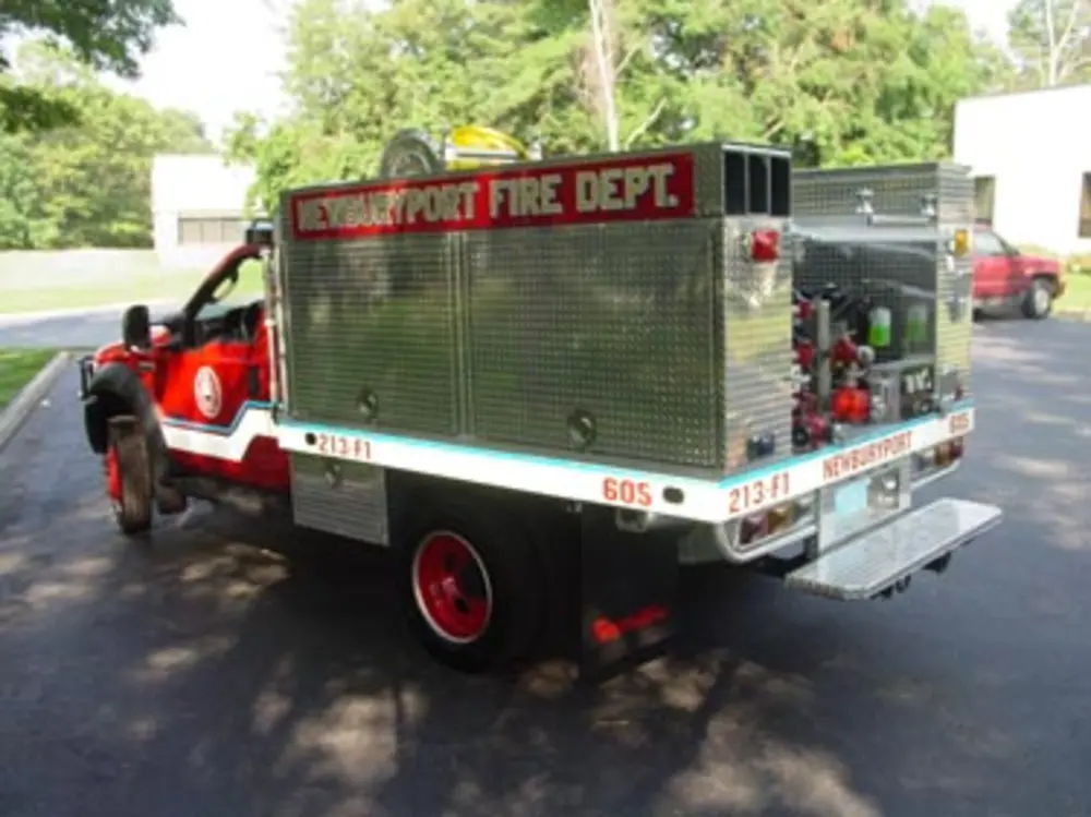 Exterior view of small fire truck showing cab, body compartments, and wheel/tire area.