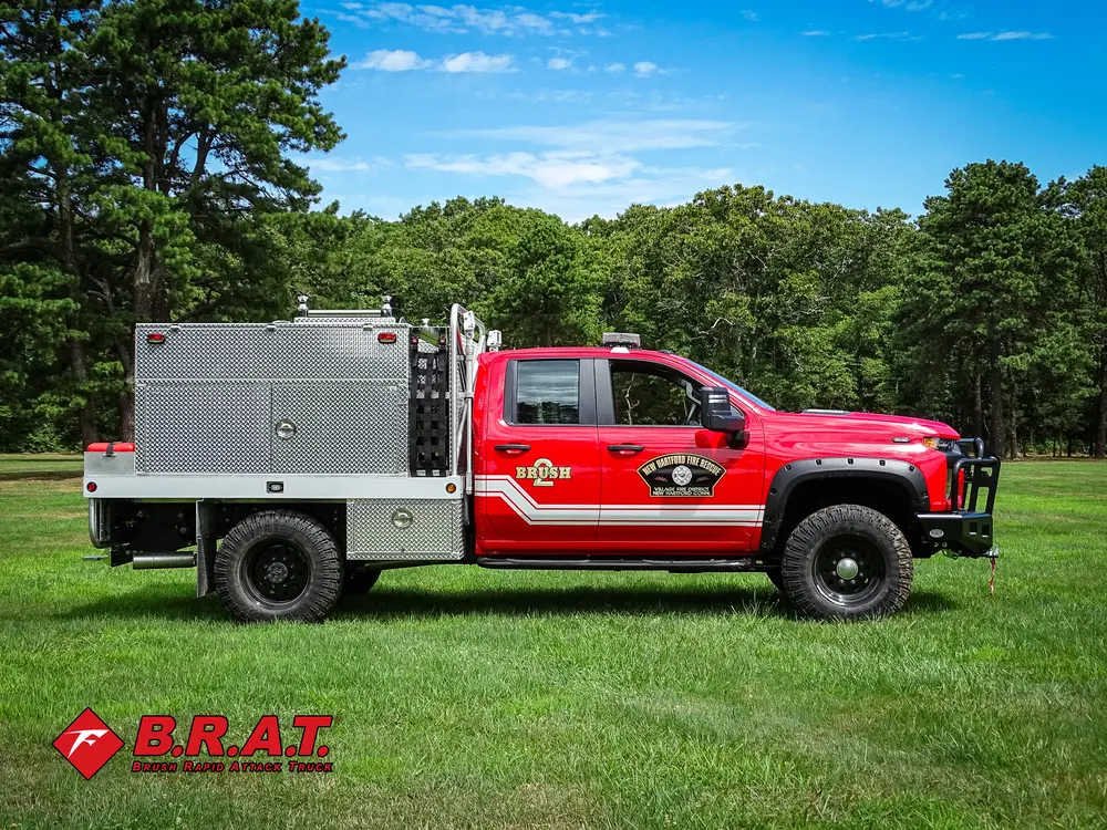 Exterior view of small fire truck showing cab, body compartments, and wheel/tire area.
