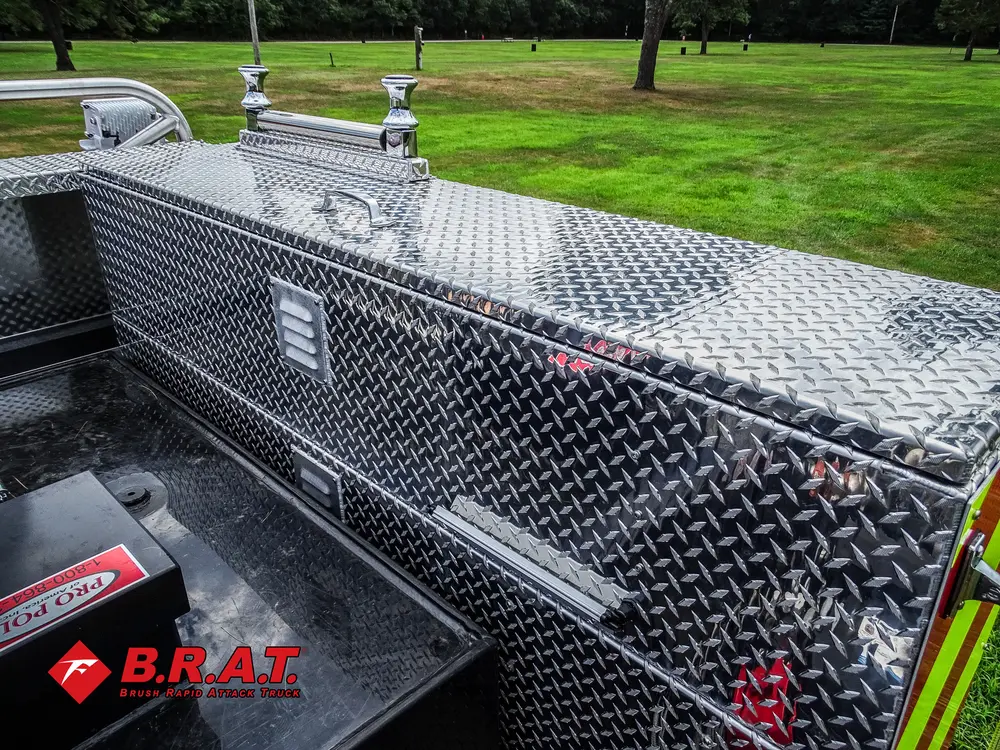 Exterior view of small fire truck showing cab, body compartments, and wheel/tire area.