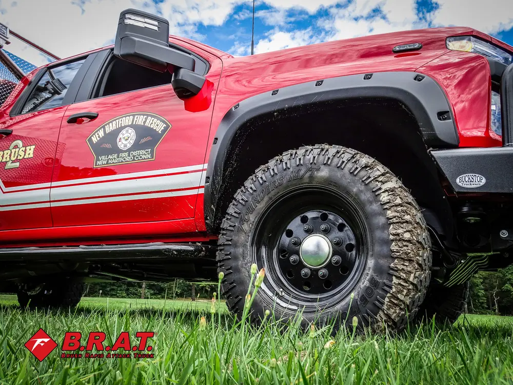 Exterior view of small fire truck showing cab, body compartments, and wheel/tire area.