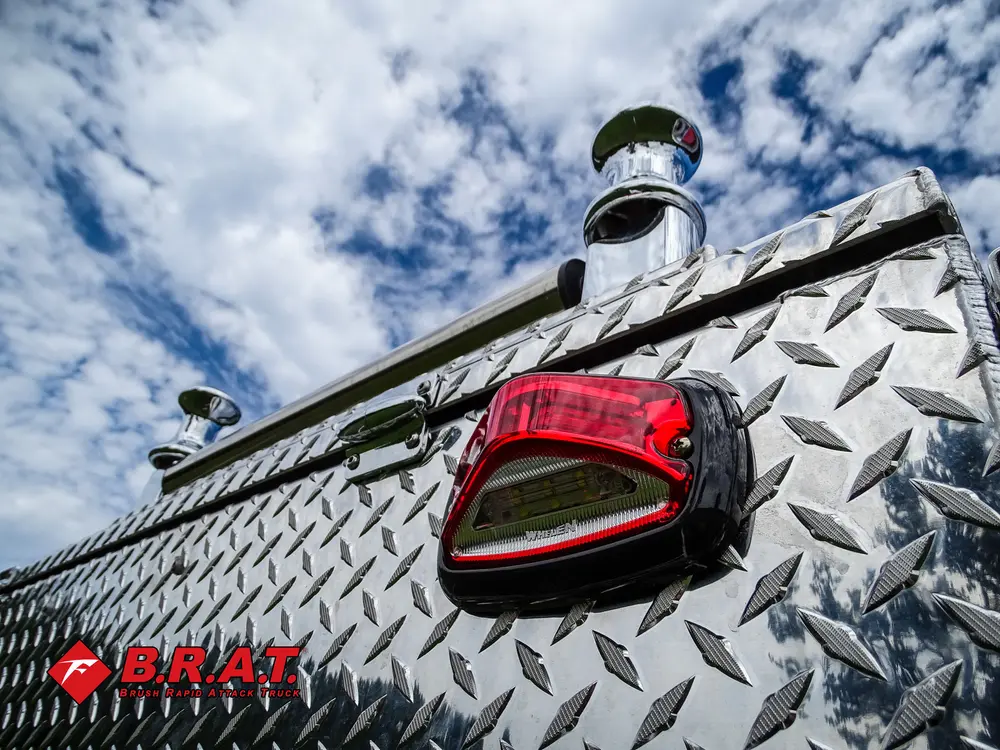Exterior view of small fire truck showing cab, body compartments, and wheel/tire area.